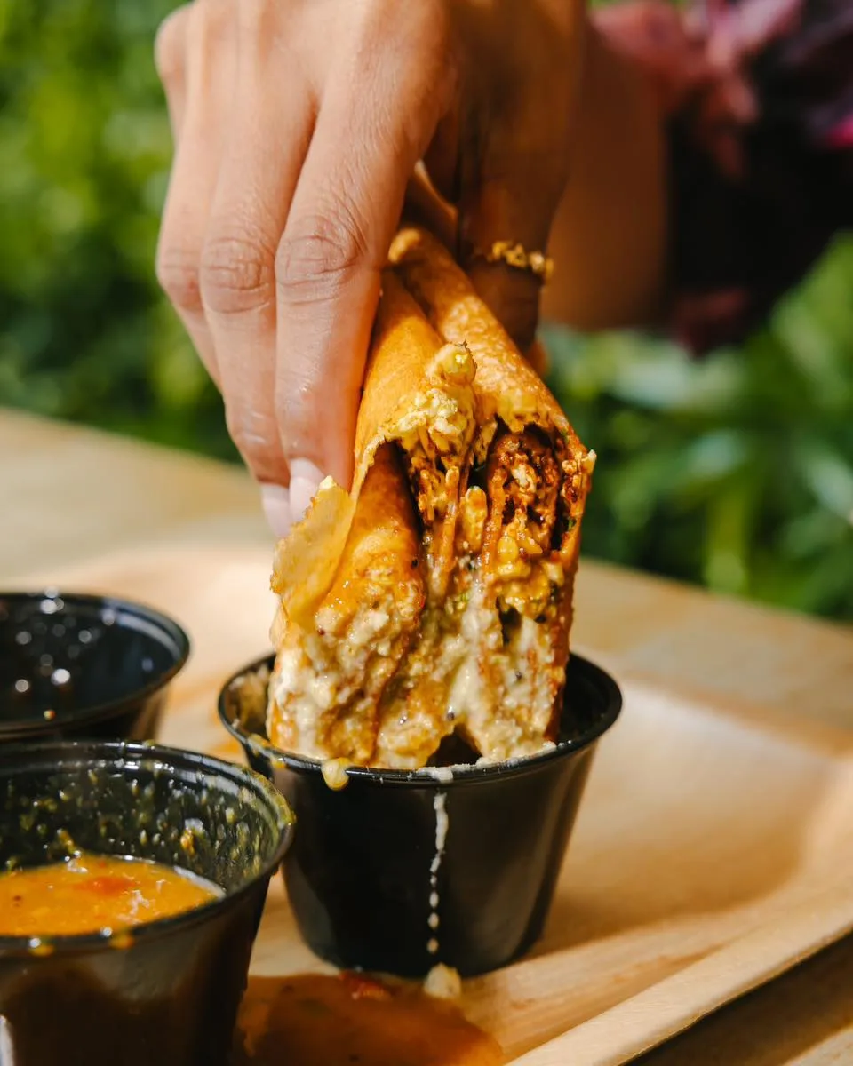 A crisp dosa being dipped into a cup of chutney