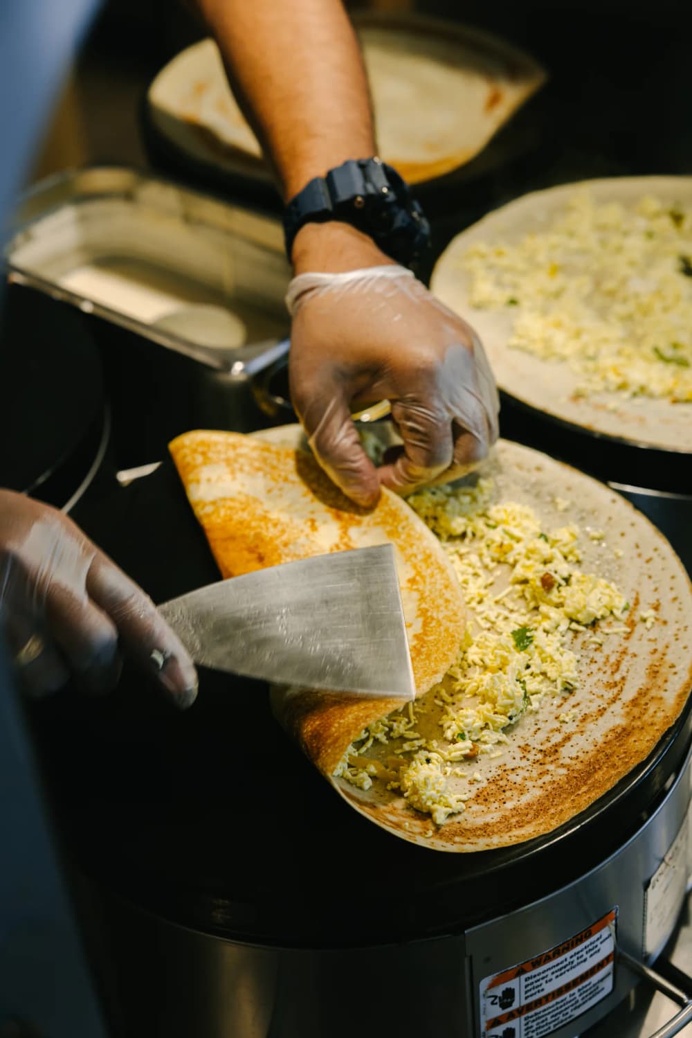 A cook folding a dosa over its filling with a spatula on the griddle