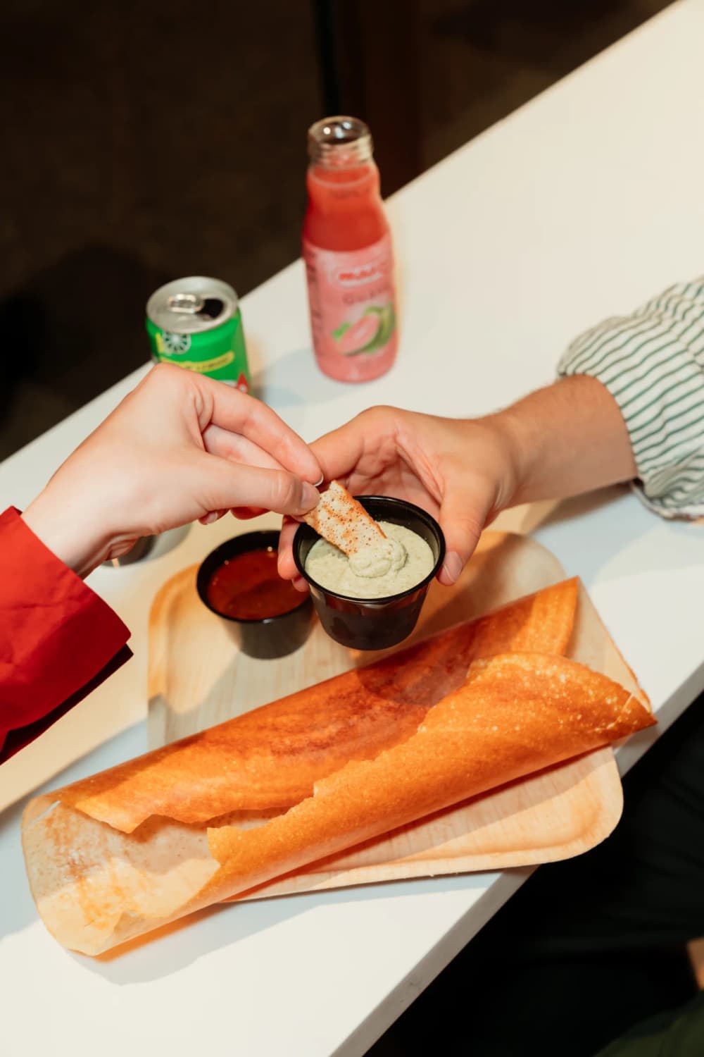 Friends sharing a crisp dosa and dipping into chutney