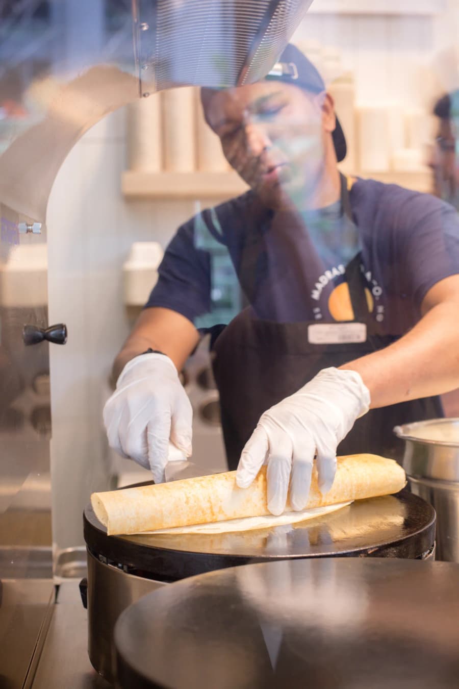 A Madras Dosa Co cook rolling a crisp dosa on the griddle