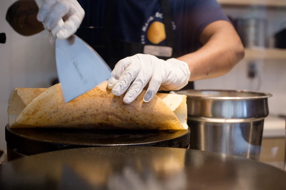 A cook folding a large, crisp golden dosa with a spatula
