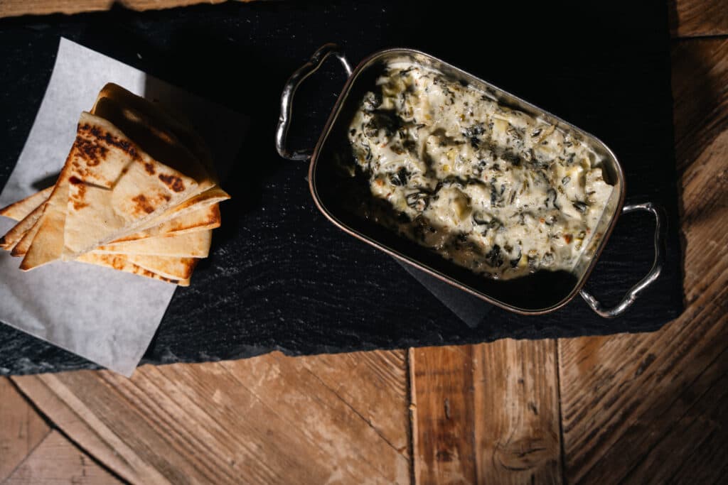 Spinach and artichoke gratin with toasted flatbread, a shareable dish from The Addison catering menu in NYC