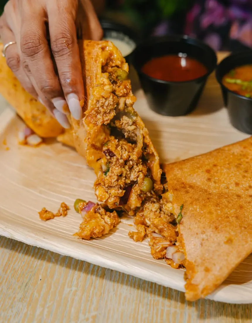 Dosa cut open to show a spiced filling, with chutneys on the side